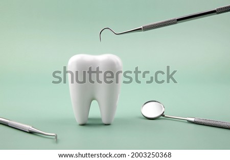 Dental explorer probe with dentist mirror and healthy tooth model on green background. Royalty-Free Stock Photo #2003250368
