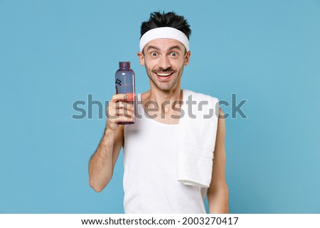Excited cheerful young strong sporty fitness man with thin skinny body sportsman in headband shirt shorts hold bottle of water isolated on blue background studio. Workout gym sport motivation concept