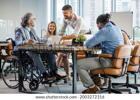 Selective focus of smiling disabled businessman and colleagues in office. Side View Of A Disabled Businessman. Young businessman greeting handicapped business partner and team. Coworker on wheelchair