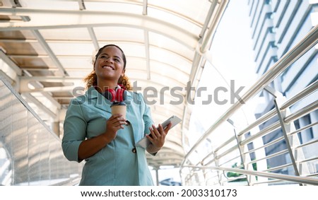Portrait of young business woman way to work on city street with tablet and headphones. Walking outdoors and working outdoors. Positive thinking. Royalty-Free Stock Photo #2003310173