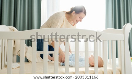 Little baby boy lying in cradle and looking at his smiling mother. Concept of parenting, family happiness and baby development