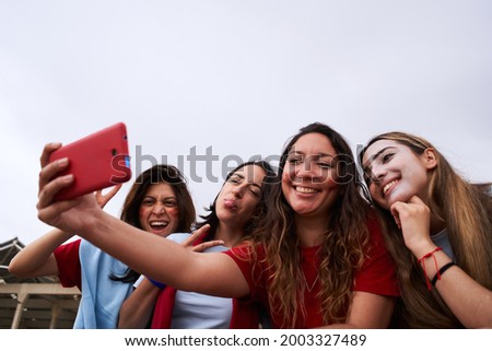 Group of female soccer fans taking selfies of themselves wearing team jerseys. Women taking pictures during the soccer match.