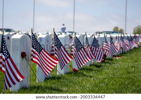 Flags on grave stones for memorial day remembrance at a cemetery. View of row of headstones with American flags. Royalty-Free Stock Photo #2003336447