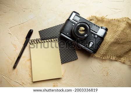 flat lay with spiral notepad, pen and camera on textured beige background. space for text