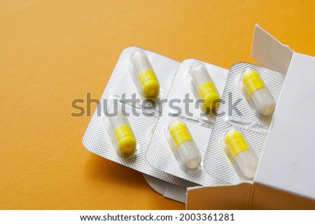 Silver blisters with yellow and white medical capsules lie in a white packing box on a yellow background. Free space for an inscription. Selective focusing. Macro