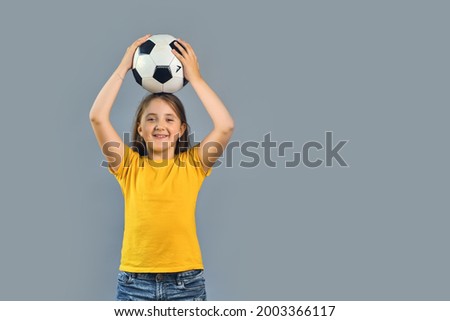 Fan sport girl player holding a ball on her head, happy smiling kid in yellow t-shirt on grey background, free text copy space