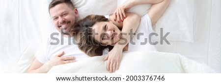 Smiling and happy man and woman lie in an embrace on bed