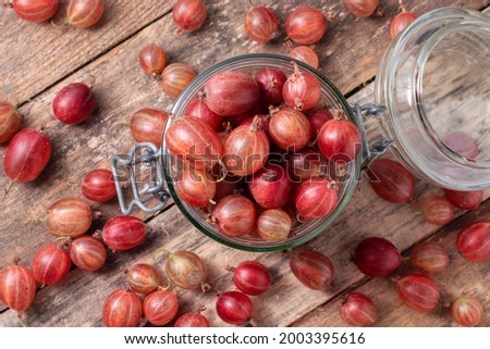 
Red gooseberries in a glass jar on a wooden background, top view.