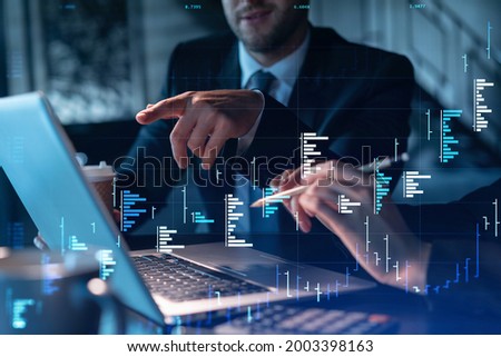 Two colleagues in formal wear working together to optimize trading strategy at corporate finance fund. Forex chart hologram over modern office background Royalty-Free Stock Photo #2003398163