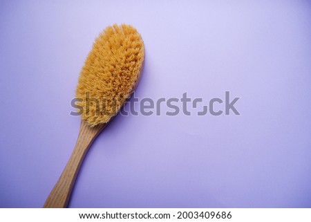Massage brush for the body.  Wooden brush made of cactus fiber on a purple background. Home body care.  Brush for anti-cellulite massage. Photo from above.