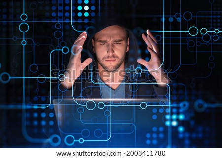 Handsome businessman in hoodie at workplace working with laptop to optimize development by implying new technologies in business process. Hi tech hologram over office background