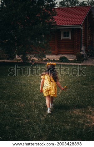 rear view of the back of a running preschool girl in a yellow dress in the backyard on a summer day. 