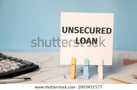 Business photo shows text unsecured loan on a sticker on office table with calculator and reports