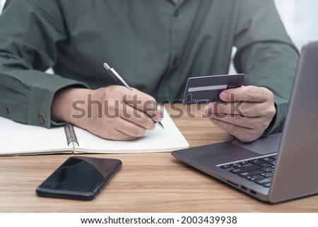Businessman hold credit card in hand for make online banking, making a payment or purchasing on the internet entering memo details on note book and laptop computer on table