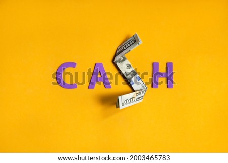 CASH. Word sign with a folded one hundred dollar bill on yellow background. 