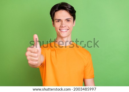 Photo of positive happy young cheerful man show thumb up recommend advertise isolated on green color background