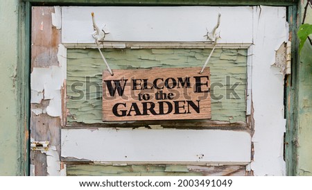 Rustic welcome garden greeting sign hanging on wooden board old shed door vintage weathered background. Welcome to the garden black text wallpaper 