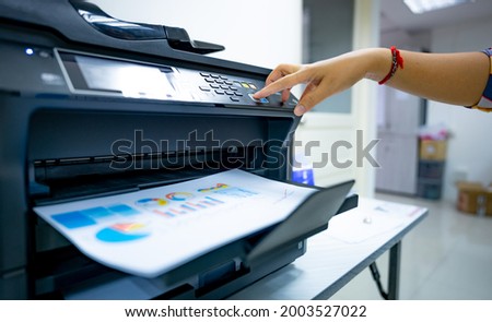 Office worker prints paper on multifunction laser printer. Copy, print, scan, and fax machine in office. Document and paper work. Print technology. Hand press on photocopy machine. Scanner equipment. Royalty-Free Stock Photo #2003527022