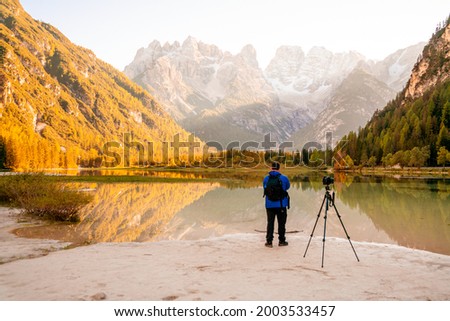 Travel photographer takes pictures of the mountain landscape. A majestic lake in the alpine mountains. Breathtaking views of the alps. A tourist is filming with a tripod.