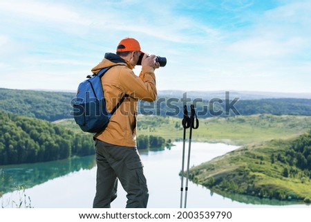 Man hiker with backpacks relaxing and taking photos during trek on top of the mountain.