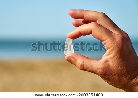 A person holds a single piece of white sea glass between their finger and thumb Royalty-Free Stock Photo #2003551400