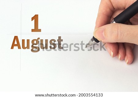 August 1st . Day 1 of month, Calendar date. The hand holds a black pen and writes the calendar date. Summer month, day of the year concept