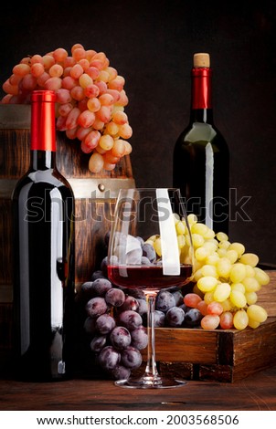 Wine bottles, grapes, glass of red wine and old wooden barrel