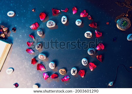 Astrology and horoscope. Stones with the signs of the zodiac, laid out in a circle, decorated with rose petals. Flat lay. The concept of divination and magic. Royalty-Free Stock Photo #2003601290
