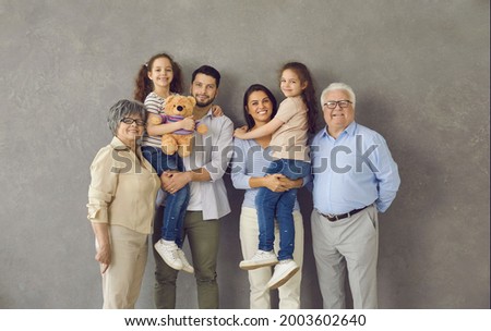 Studio photo shoot group portrait of cheerful big extended multi generational family against grey background.Happy smiling mom, dad, grandma, grandpa and two little kids all together looking at camera Royalty-Free Stock Photo #2003602640