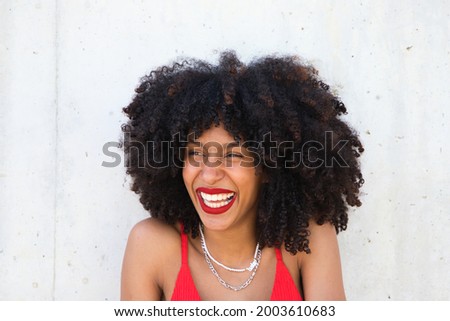 beautiful afro american woman smiling and looking at the camera doing different poses and gestures with her face. The woman is wearing a red top and red lipstick. Concept happiness Royalty-Free Stock Photo #2003610683