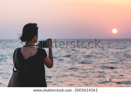 Young asian girl is taking a photo with vintage camera in sunset time on the beach.