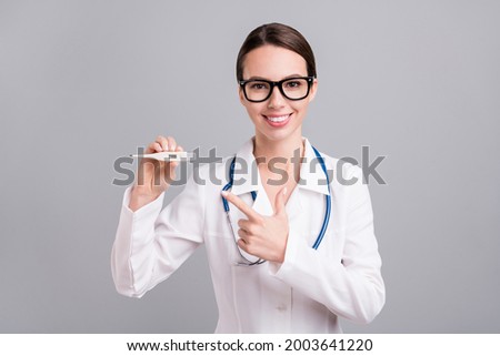 Photo of positive sweet young doc woman dressed white coat spectacles pointing finger thermometer isolated grey color background