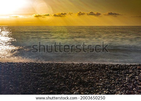vivid photo of the sea sunset. The sky in rays of sunset against background of sea and pebble beach