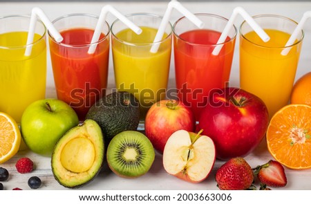 Different fruits juice in glass, apple, orange and strawberry juice with straw, looking refreshing on colourful wood board in front of white wall background. Picture decorating with fresh fruits.