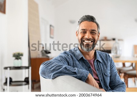 Portrait of handsome mature man relaxing on couch at home while looking at camera. Mixed race man in casual clothing sitting on sofa and smiling with copy space. Successful happy middle eastern guy. Royalty-Free Stock Photo #2003674964