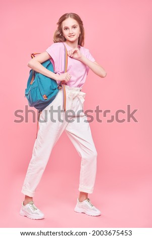 School time. Full length portrait of a carefree pretty girl teenager in light summer clothes and with backpack posing at studio on a pink background. Youth fashion. 