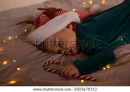little baby lies on the bed in a Christmas costume and a hat with deer antlers. Christmas and new year