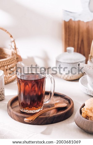 A glass of tea next to tea pot, creamer and others in bright harsh light. Tea time situation.