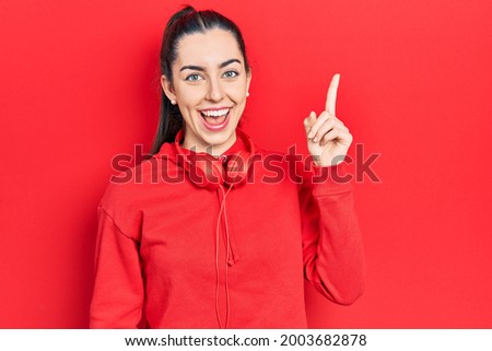 Beautiful woman with blue eyes wearing gym clothes and headphones pointing finger up with successful idea. exited and happy. number one. 