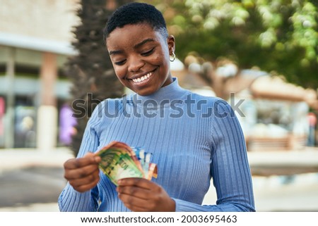 Young african american woman smiling happy counting south africa rand banknotes at the city. Royalty-Free Stock Photo #2003695463