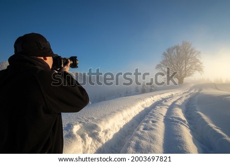 Hiker photographer taking pictures of snowy nature in winter mountains.