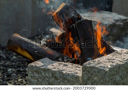 Cined campfire with wooden logs, surrounded by granite stones. Man senses the heat and hears the crackling of the burning wood.
