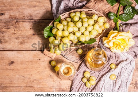 White wine and grape in a wicker basket. Fresh fruits, glass, and bottle. Modern hard light, dark shadow. Old wooden boards background, top view