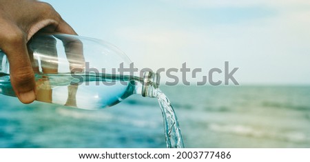 closeup of a young caucasian man pouring water from a reusable water bottle in front of the sea, in a panoramic format to use as web banner or header Royalty-Free Stock Photo #2003777486