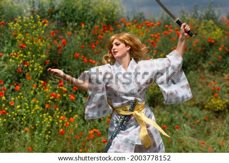 Young asian woman in traditional kimono trains fighting techniques with katana sword on the hills with red poppies, samurai warrior girl