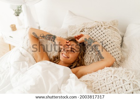 Laughing woman chilling in her bed. Tatoo on hends. Cozy home lifestyle. 