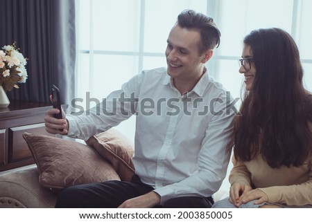 Happy young couple sitting on a couch at home, using mobile phone