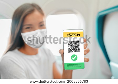 COVID-19 Vaccine passport on mobile phone app screen woman wearing mask on flight showing vaccination proof at arrival to airport for vacation travel flying during coronavirus pandemic.