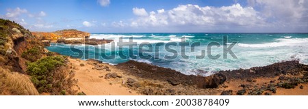 The Australian rocky coast is about 12 apostles. Strong winds drive ocean waves to the shore cliffs. A wide panorama. Sand dunes and cliffs. Blue sky with clouds on the horizon. Royalty-Free Stock Photo #2003878409