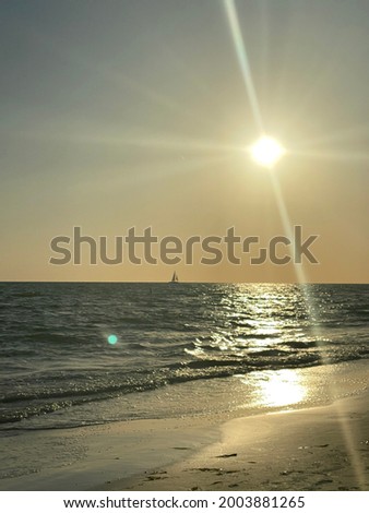 Unfocused photo of the sun setting in the ocean with a sailboat silhouette on the beach